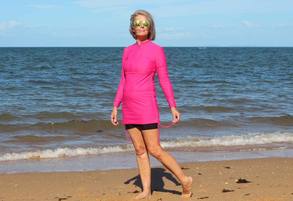 Banner- mature women wearing long pink swim shirt walking on beach