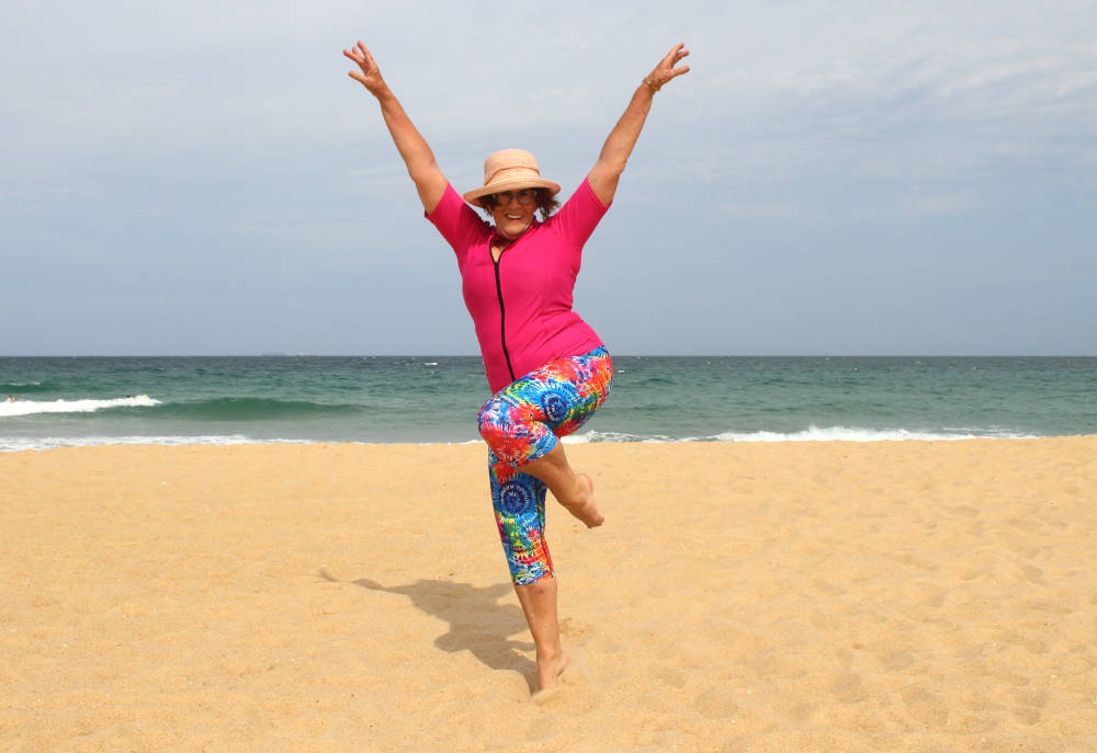 mature woman dancing on a beach in the sand wearing ocean road swimwear colourful sun safe swimsuit women empowerment