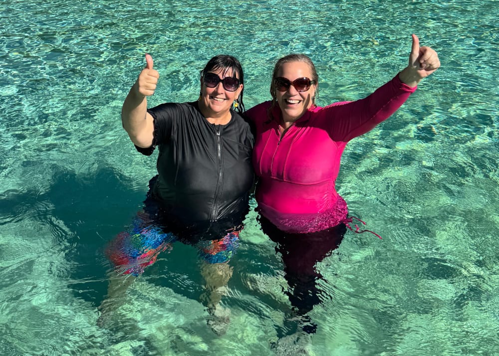 Two happy swimmers wearing OceanRoad chlorine-treated swimsuits in a pool, giving a thumbs up to show fabric durability.