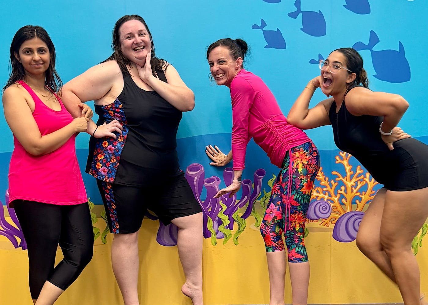 Staff and mature students laughing in front of a colorful memorial mural at JUMP! Swim Schools Richlands.