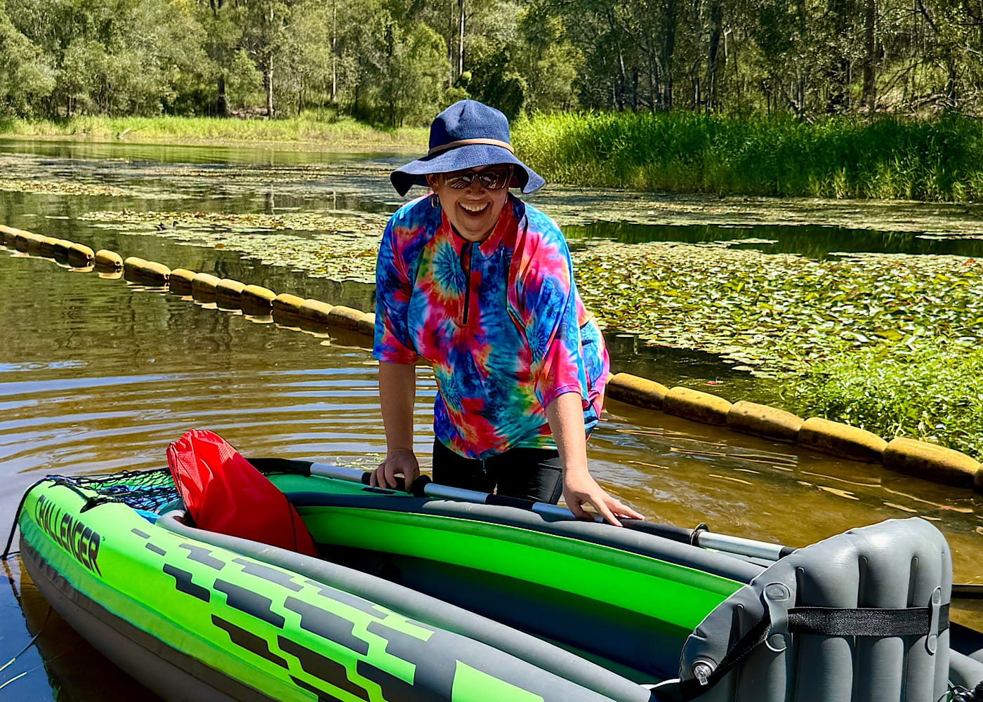 Laura Vincent leaning over a green kayak at the water's edge in floral leggings.